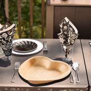 Heart-shaped palm plates styled with hors d'oeuvres for a romantic outdoor picnic with natural charm.