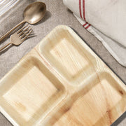 Palm leaf sectioned plates arranged with main courses and sides on a rustic table for eco-friendly dining.