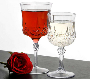 Two elegant crystal wine glasses, one filled with red wine and the other with white wine, rest on a dark wooden surface. A single red rose lies beside the glasses, adding a touch of romance and sophistication to the scene.