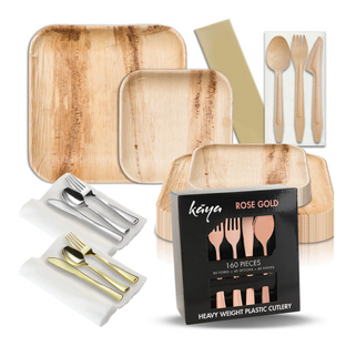 A collection of eco-friendly dinnerware and cutlery sets including square wooden plates in different sizes, wooden cutlery, gold and silver metal cutlery sets wrapped in white cloth napkins, and a box of rose gold heavy plastic cutlery labeled