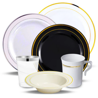 A collection of various tableware items includes two dinner plates, one white with a gold rim, and one black with a gold rim, a white bowl with a gold rim, a clear glass with a silver rim, and a white mug with gold detailing.