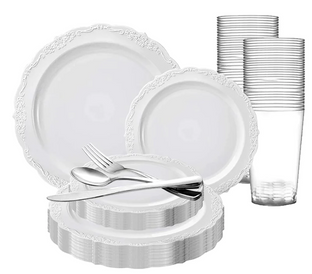 A set of white plastic plates with intricate borders, accompanied by multiple clear plastic cups. In the foreground, there are plastic cutlery items including a spoon, fork, and knife. The items are stacked and arranged neatly.