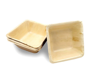A stack of eco-friendly, square-shaped wooden plates. The plates have a light natural wood color and a smooth texture. Three plates are partially stacked, with one plate resting on top, slightly offset from the others.
