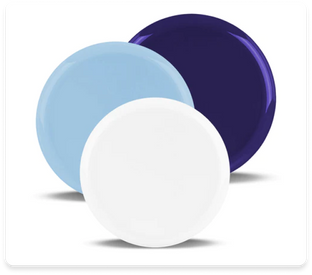 Image of three round porcelain plates arranged to partially overlap each other. The plates are colored light blue, purple, and white, positioned from left to right. Each plate casts a faint shadow on the surface behind them.