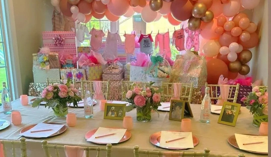 Baby shower table adorned with pink and gold balloons and disposable party supplies.