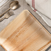 10" square palm leaf plates featured at a sustainable dinner setup with candles and wooden utensils.