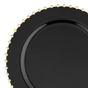 The Black with Gold Pearl String Round Disposable Plastic Salad Plate (7”) showcases a glossy black finish adorned with a row of evenly spaced, small, gold-colored beads along its outer rim, adding an elegant touch to its simple design. This sophisticated plastic plate is presented against a plain white background.