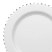 A partial view of a White with Silver Pearl String Round Disposable Plastic Salad Plate showcases its circular design with a raised, silver pearl string rim. This 7-inch, BPA-free plate boasts a smooth and glossy finish while the evenly spaced beads add an elegant decorative touch to its edge.