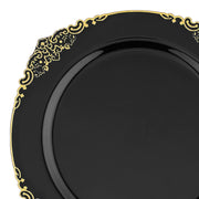 The Black with Gold Fancy Round Disposable Plastic Dinner Plate (10.25") features an ornate gold pattern adorning the outer rim. The detailed design includes intricate swirls and flourishes, adding an elegant touch to the simple, glossy surface of the plate. This photo captures just over three-quarters of these elegant round disposable plates.