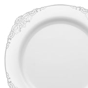 A White with Silver Fancy Round Disposable Plastic Dinner Plate (10.25") featuring an intricate, delicate floral pattern along the edge is showcased. The design is subtle and elegant, giving the plate a classic and refined appearance. The plate is empty and set against a plain background.