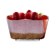 A dessert in 5.5 oz. clear fluted rectangular disposable plastic pudding cups, featuring a crumbly, thick crust base topped with a smooth pink filling and garnished with a glossy red glaze and fresh raspberries.