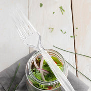 Clear medium heavy weight plastic forks set beside plates at a party table, sleek disposable flatware for weddings, showers, and receptions.
