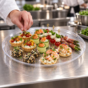 Disposable 18-inch round clear plastic serving tray showing durable crystal-look design with fruit display.