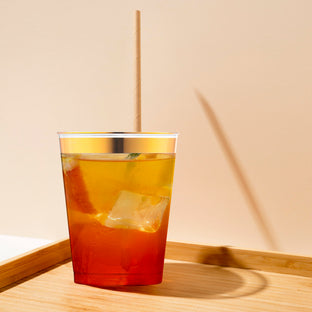 Elegant clear plastic tumbler with gold rim filled with iced tea, sophisticated disposable drinkware for summer parties and events.