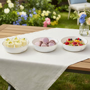 Elegant white disposable plastic serving bowls with gold rim filled with appetizers at a cozy indoor family gathering.