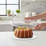 Hand holding a 12 inch clear high dome plastic lid over cupcakes, transparent snap-on cover to protect dessert decorations during transport.