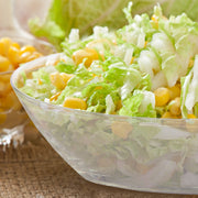 Hand squeezing lemon over a fresh salad in a large clear oval plastic serving bowl, perfect for catering and party food preparation.