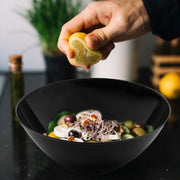 Solid Black Organic Round Disposable Plastic Bowl (100 oz.) elegantly served with fresh salad, olives, and onions.