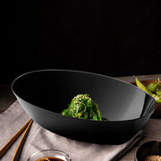 Stylish black oval plastic salad bowl with fresh ingredients, modern disposable party supplies for elegant buffet presentations.