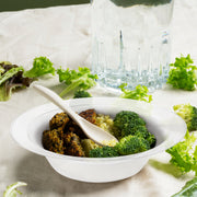 Transparent plastic bowl filled with seasoned broccoli, grains, and meat for tasting setup