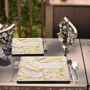 White square plates with golden marble pattern arranged for an upscale garden event with wood accents.